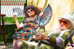 Two hip old ladies cool themselves with tall drinks and hand fans.