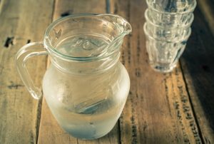 A jug filled with water and empty stacked cups on wooden table.