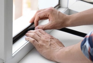 hands applying a strip of black insulation to window