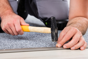 hands hammering tack into carpet edge
