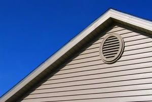 Exterior view of a gable vent on a white-sided house against a blue sky.
