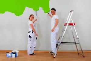 A couple painting a wall green.