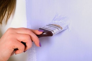 A woman's hand paints a wall violet with a paintbrush.