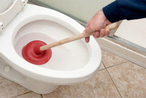 A man using a red plunger to try to unclog a toilet.