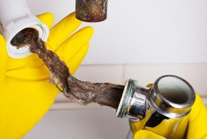 gloved hands unclogging sink drain