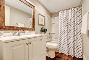 A bathroom with a framed mirror and white cabinet.