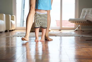 A mom teaching her baby how to walk on wood flooring. 