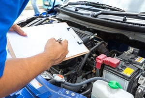A man look at an engine while writing on a clipboard.