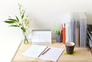 A home office desktop with files, a calendar, and a vase of flowers.