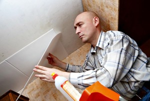 A man on a ladder installing ceiling tiles.