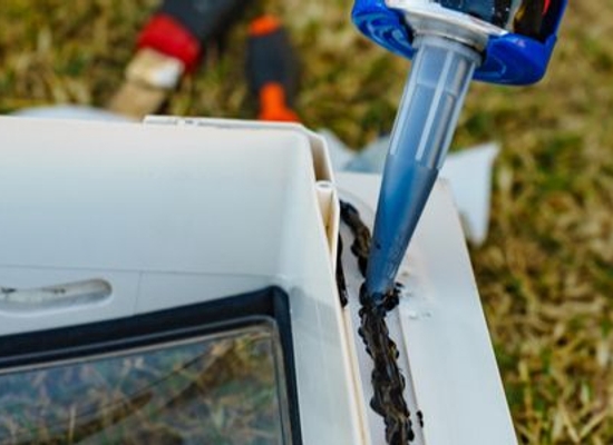 hands fixing RV window with caulking