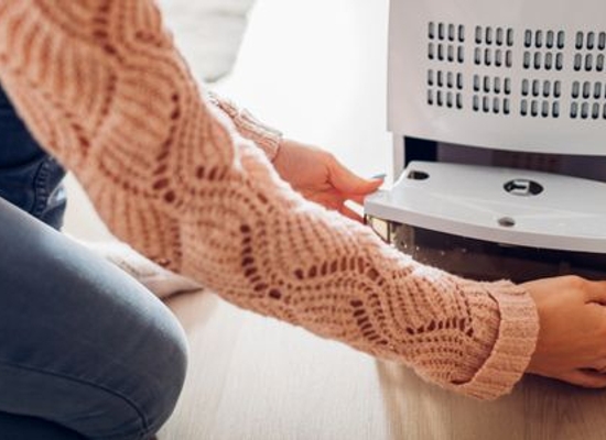 person in sweater opening the bottom of a dehumidifier