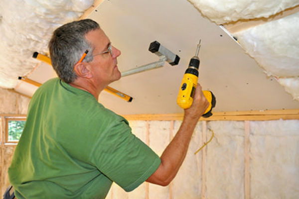 man installing drywall on a ceiling
