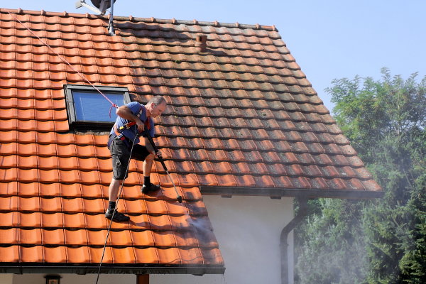 A man spraying off dirt from a red tile roof. 