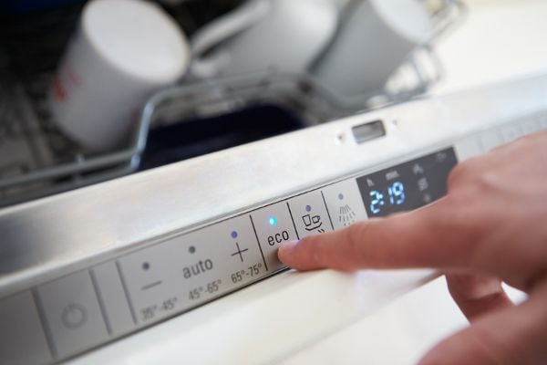 A dishwasher slightly open with a hand choosing a setting. 