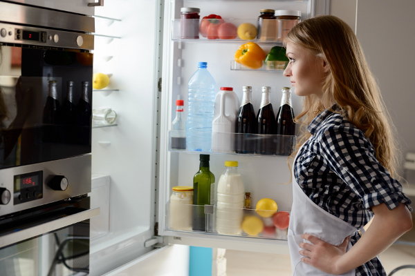 An open fridge with food and woman standing in front of it. 