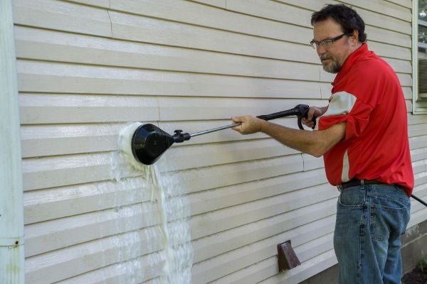 A man washing his siding with a brush. 