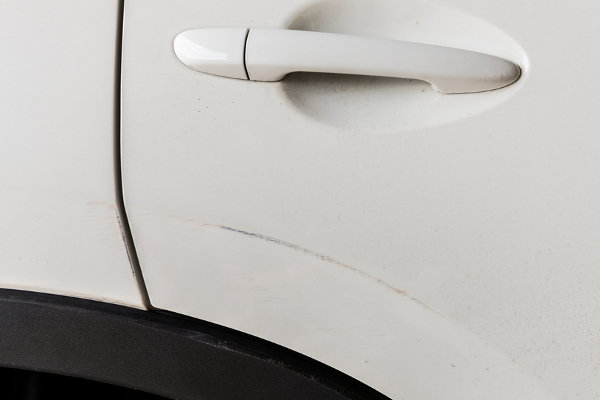 A close-up of a white car with a scratch by the handle. 