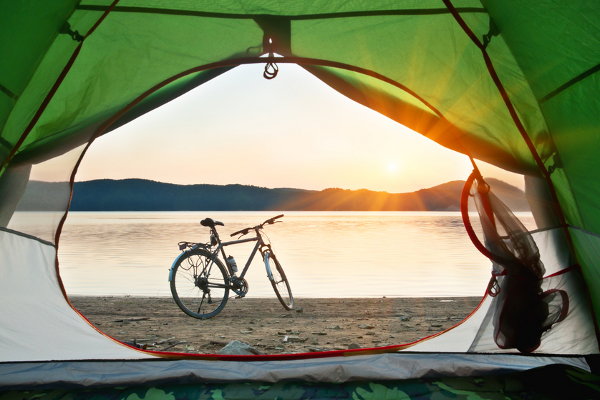A green tent opening up to a lake and a bike in the foreground. 