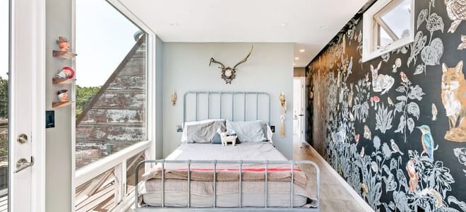 Rustic metal bed frame in a small room with animal print wallpaper and large windows