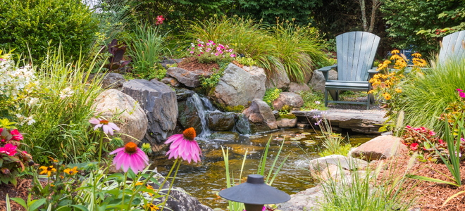 A backyard pond surrounded by chairs, large rocks, and plants