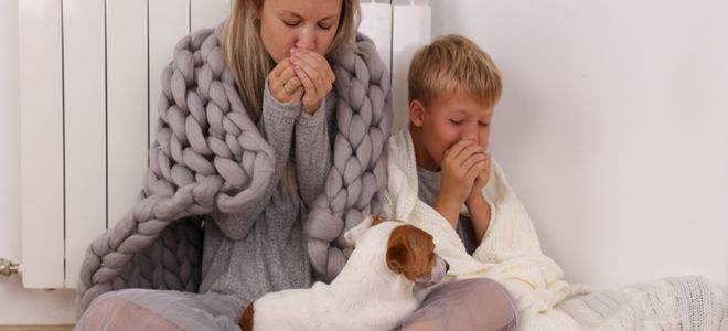 a woman, dog, and boy shivering next to a heater