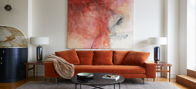Burnt orange couch, grey carpet, and large wall art in a living room