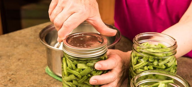 Someone twisting a lid onto a mason jar full of green beans. 