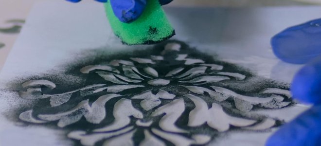 Gloved hands applying paint to a stencil