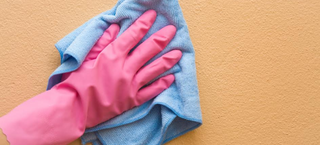 wearing a pink glove and wiping a wall with a rag