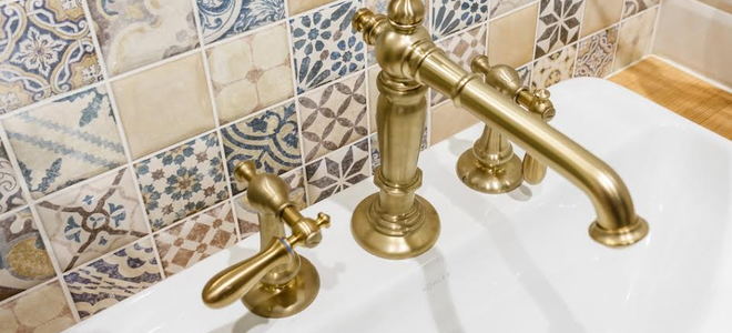 brass sink fixtures with tile on wall behind it