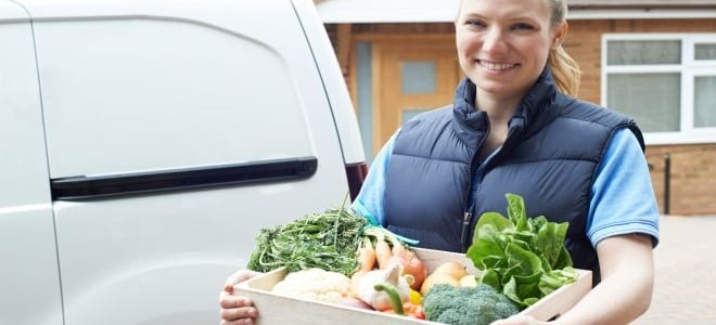 A woman holding a wood box of produce that she's going to enjoy instead of red meat on Earth Day. 