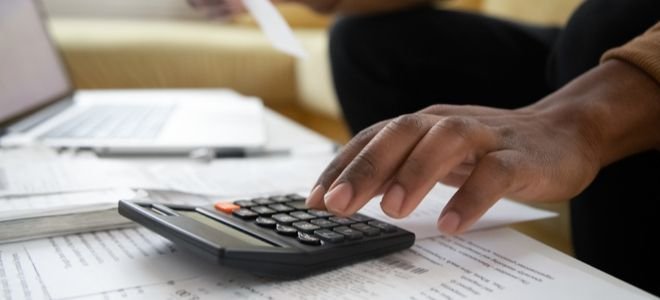 hand using calculator with laptop and papers