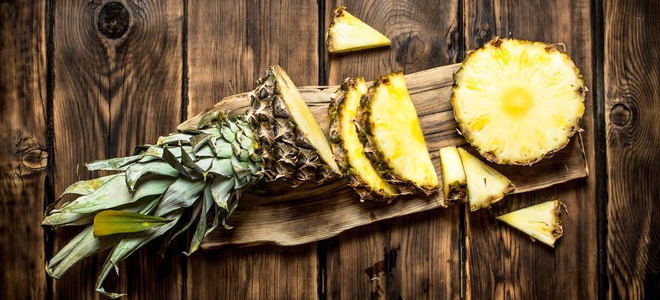 A cut pineapple on a cutting board against a wood background. 