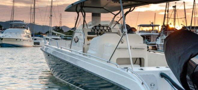 A small, fiberglass boat docked in a marina at sunset.