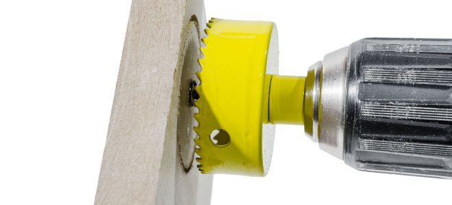 drill with circle saw cutting hole for pipe in piece of wood