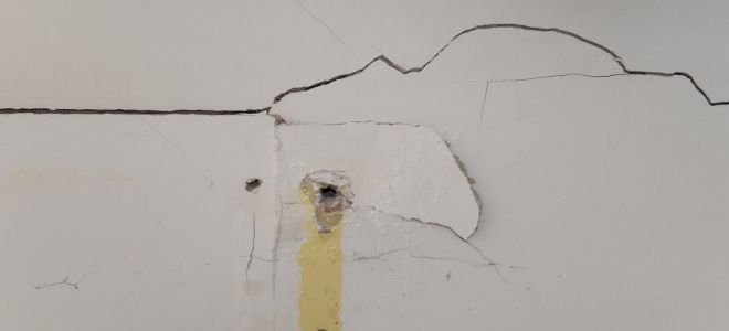 A crack and hole in drywall that needs to be repaired.