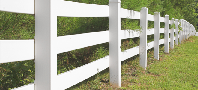 A white vinyl fence against some pine trees.
