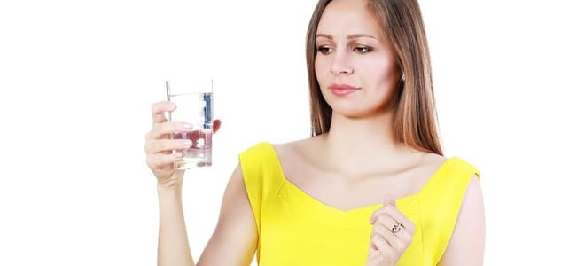 A woman holding a cup of water and looking at it with a discouraged face. 