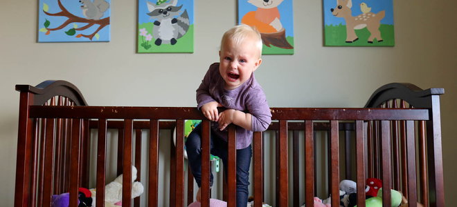 Baby leaning over the edge of a crib