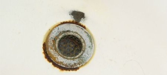 An old sink drain with rust around the metal fitting.
