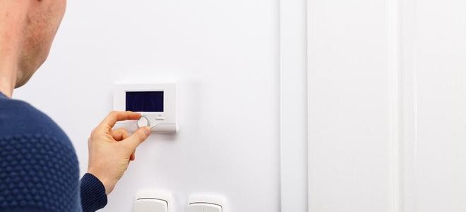 A man adjusting a thermostat on a white wall.