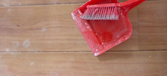 A red dust pan and broom on wood flooring. 
