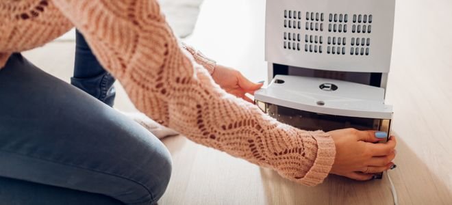 person in sweater opening the bottom of a dehumidifier