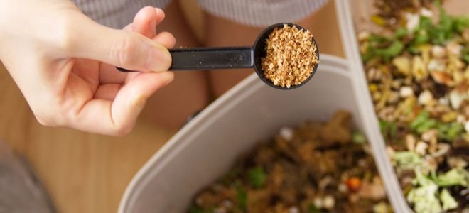 hand adding scoop of bokashi additives to compost bucket