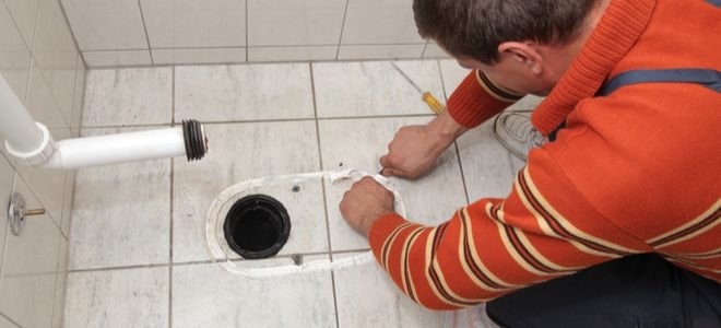 man scraping caulking from old toilet placement