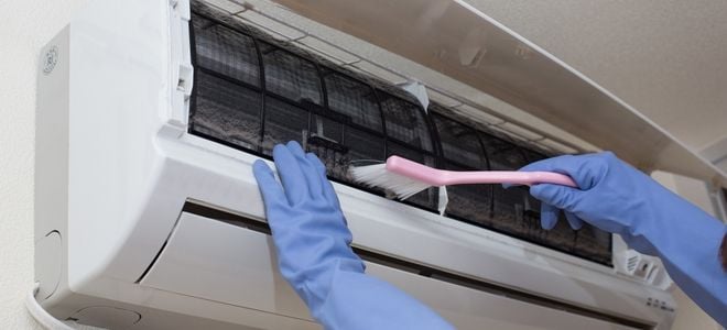 gloved hands cleaning a wall mounted air conditioner