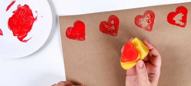 a hand applying red heart stamps to brown paper