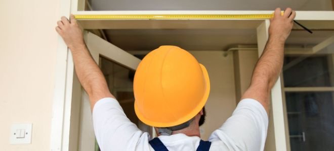 man in hard hat measuring door frame