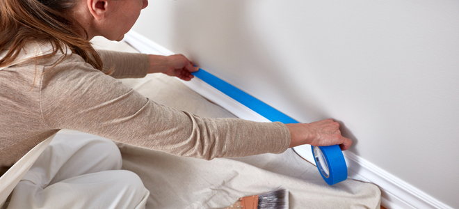 person applying tape to a baseboard to protect from painting